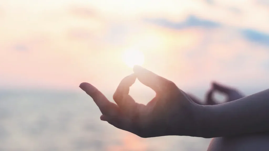朝日が昇る海で瞑想をする。ムードラの両手。
