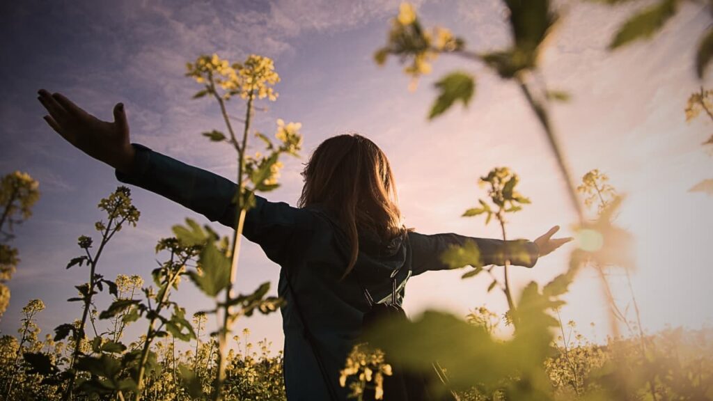 自然の中で両腕を広げ、光を浴びながら立っている人物の後ろ姿